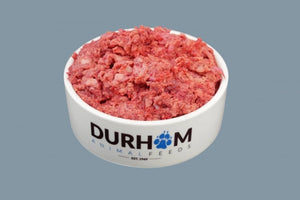 A white bowl with Durham Animal Feeds written on it in black and blue, containing raw lamb mince, against a pale blue background.