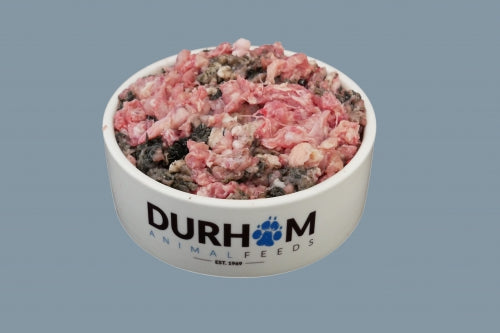 A white bowl with Durham Animal Feeds written on it in blue and black, containing raw turkey and tripe mince, against a pale blue background.